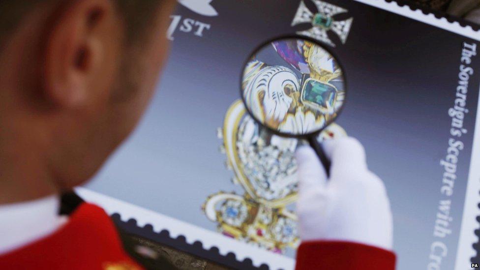 A man inspecting one of the crown jewel stamps with a magnifying glass.