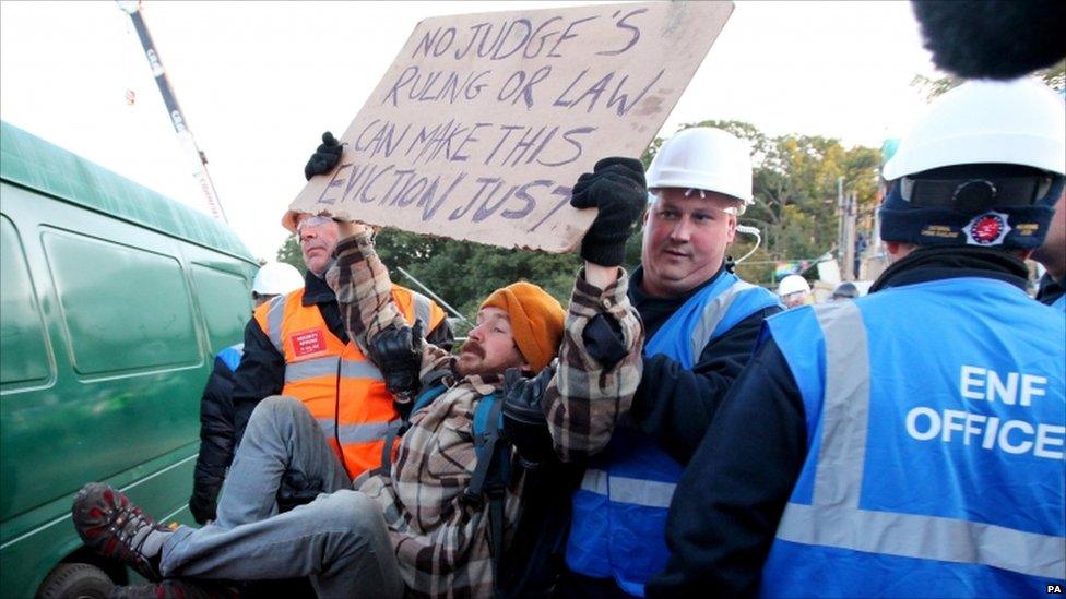 An Enforcement Officer and a Security Officer remove a protester at Dale Farm in Essex where supporters have clashed with riot police at the UK"s largest illegal travellers" site as the planned eviction got under way on 19 October