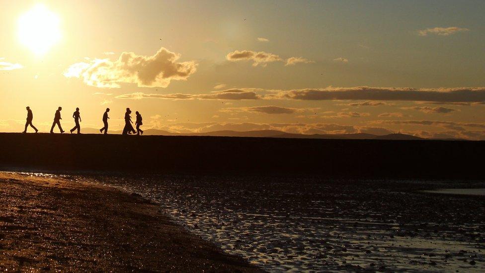 People walking on Cramond beach in Edinburgh as the sun sets