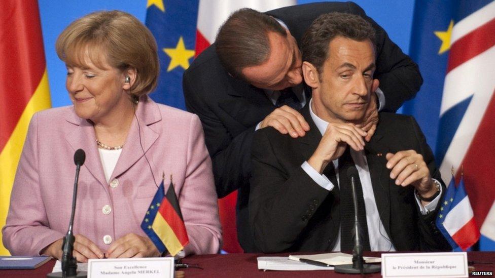 Silvio Berlusconi talks to French President Nicolas Sarkozy as German Chancellor Angela Merkel looks away in Paris, 4 October 2008