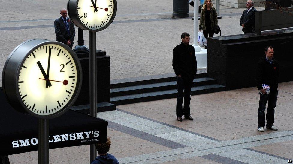 Clocks at showing 11.01am, beside people standing still.