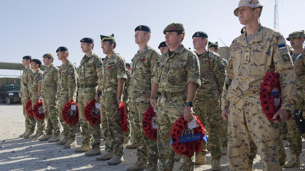 Soliders standing on sandy ground, holding wreaths