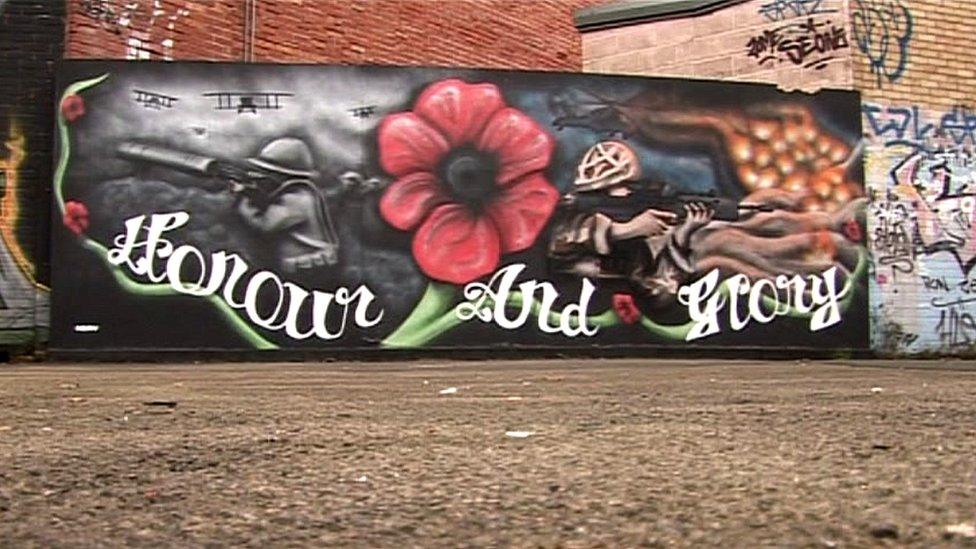 Large painting on wall saying "hope and glory" with a poppy above it, next to a soldier pointing a gun.