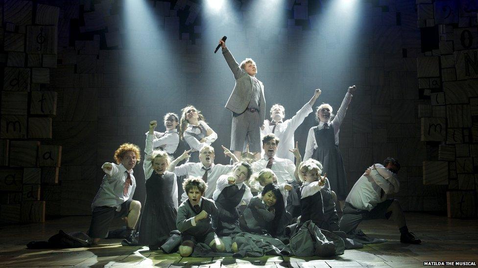 Ensemble of children hold up their hands at the end of a musical number