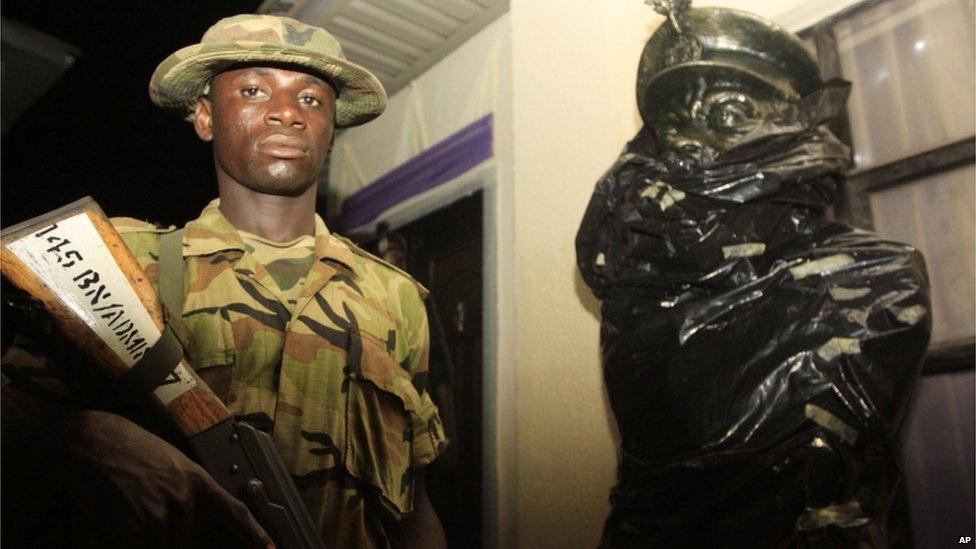 A soldier stands guard next to a partially wrapped statue of Chukwuemeka Ojukwu