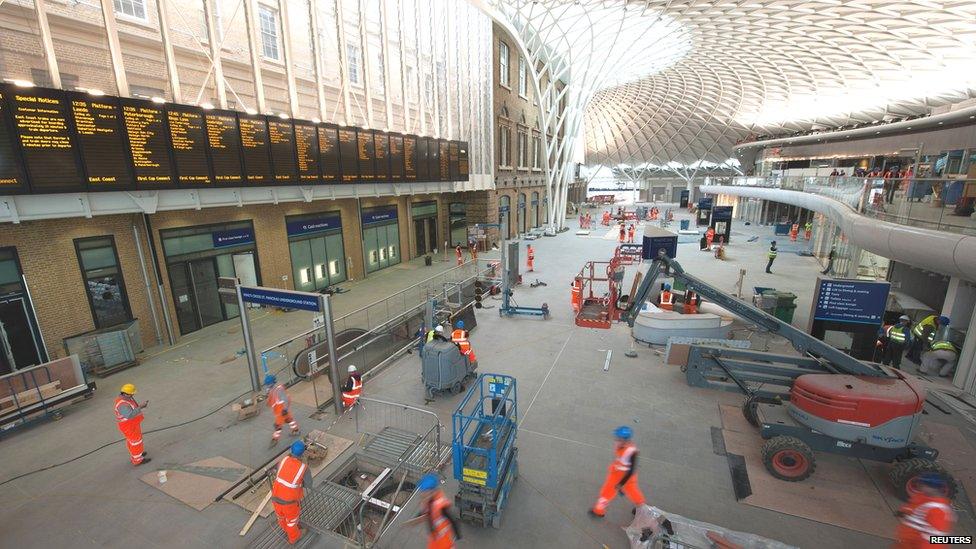 Workmen in fluorescent orange overalls are seen on the concourse, adding the finishing touches to the station.