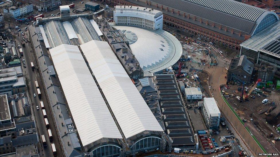 An aerial shot of King's Cross Station. Two long, rectangular enclosures house the station's platforms. To the right of these, a semi-circular concourse has been built, with a white roof.