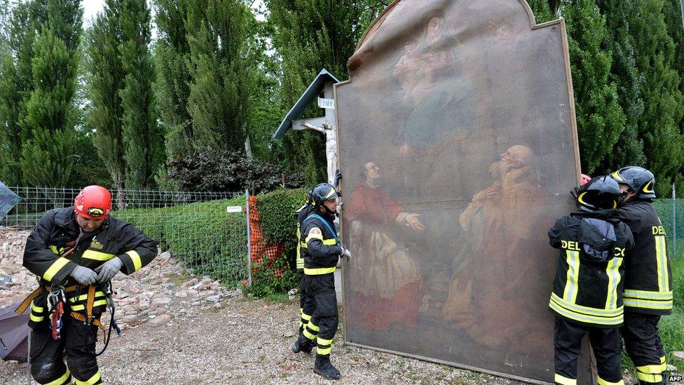 Firemen handle a painting recovered from a destroyed church in the village of San Carlo after an earthquake shook downtown Finale Emilia.