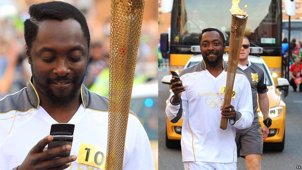 will.i.am carrying the Olympic flame whilsting texting on his mobile phone.