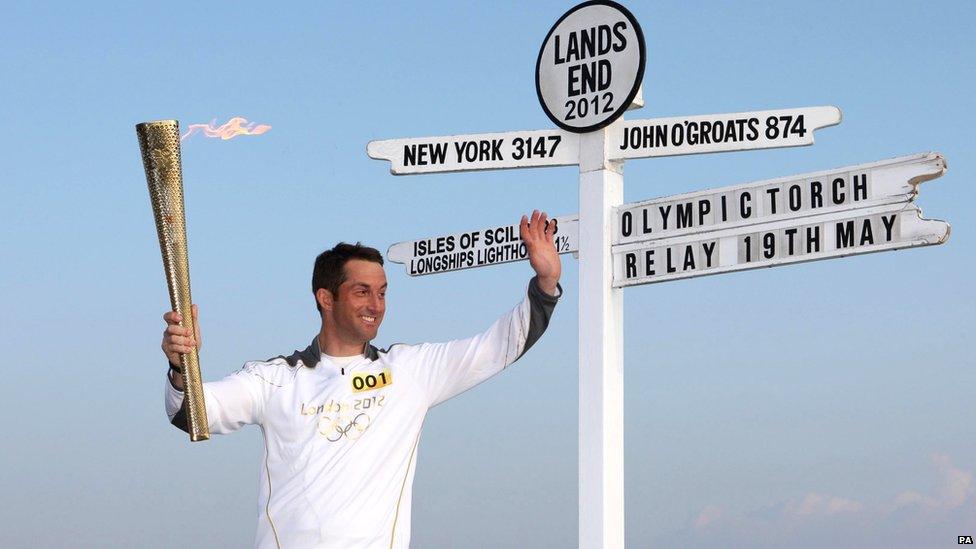 Ben Ainslie waving as he holds the Olympic torch, before he kicks off the torch relay from Land's End