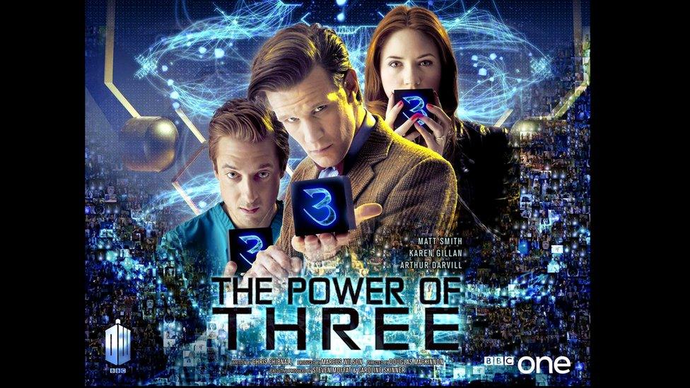 The Doctor and his companions hold cubes with the number 3 on them.