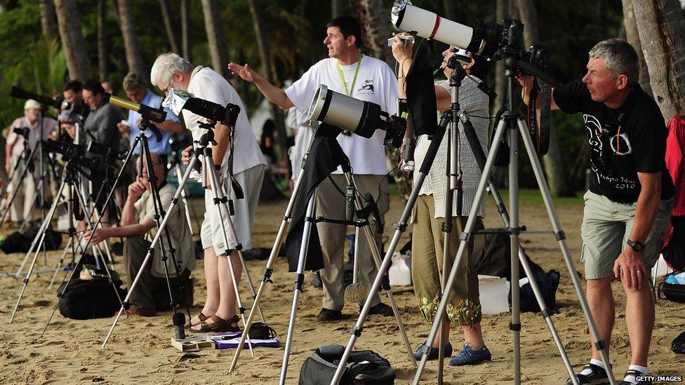 People on a crowded beach with cameras and telescopes