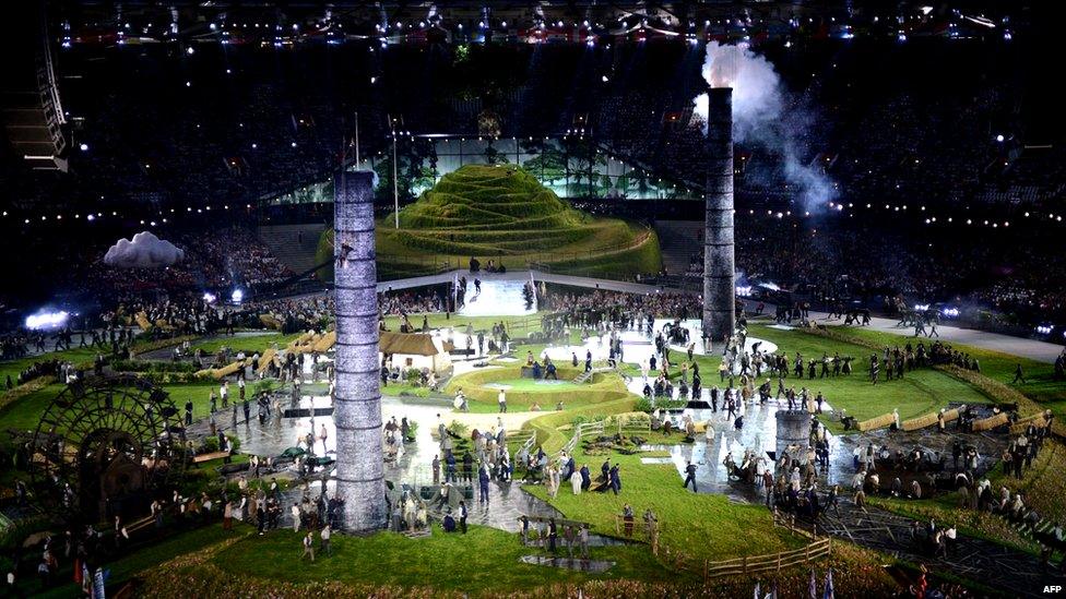 A scene from the opening ceremony of the London 2012 Olympic Games. The stadium is filled with grass and performers.