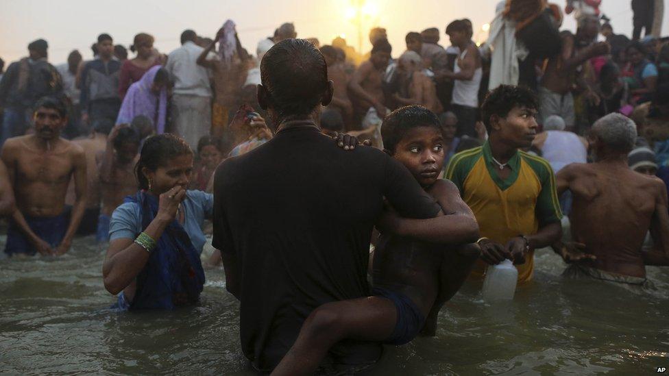 An Indian Hindu boy is held by his father as they go for a dip at Sangam, the confluence of the rivers Ganges, Yamuna and mythical Saraswati, during the royal bath on Makar Sankranti at the start of the Kumbh Mela