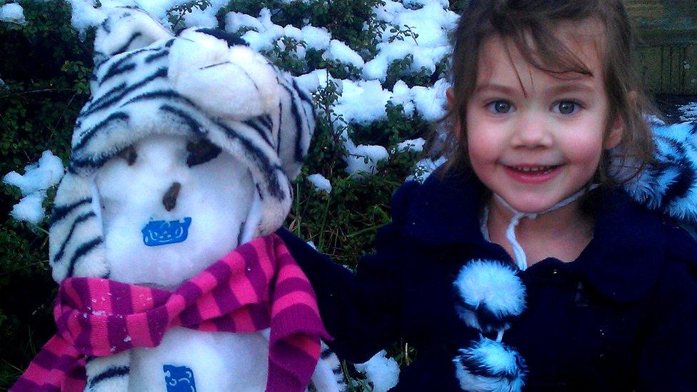 A girl sat beside her snowman.