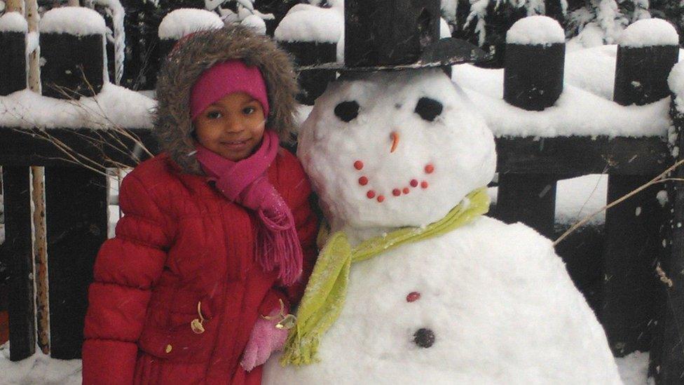 A girl with her snowman. It is wearing a top hat.