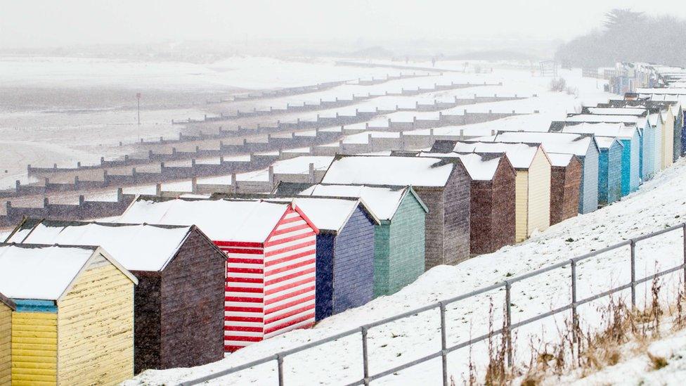 Colourful beach huts on the beach. The whole scene is covered in snow.