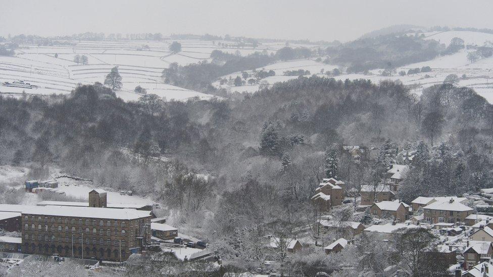 A wide view of a snowy landscape - trees and hills covered in snow. There are houses and buildings in the foreground.