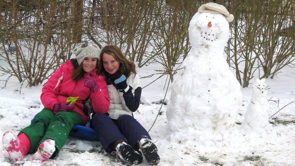 Two girls in the snow with their snowman.