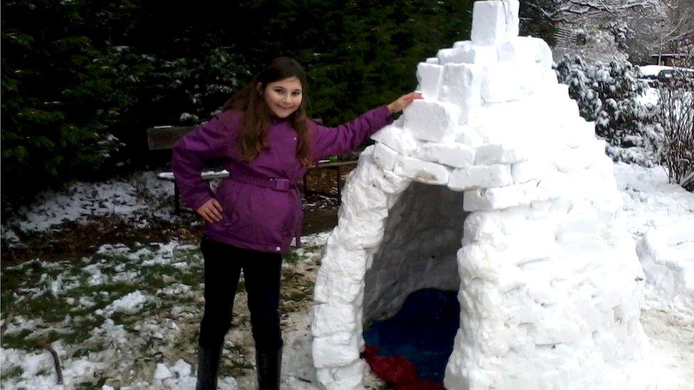 A girl stood beside an igloo.