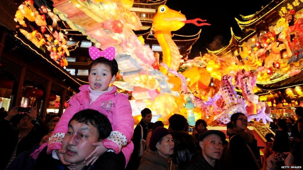 A girl on her father's shoulders in front of a giant dragon lantern in Shanghai