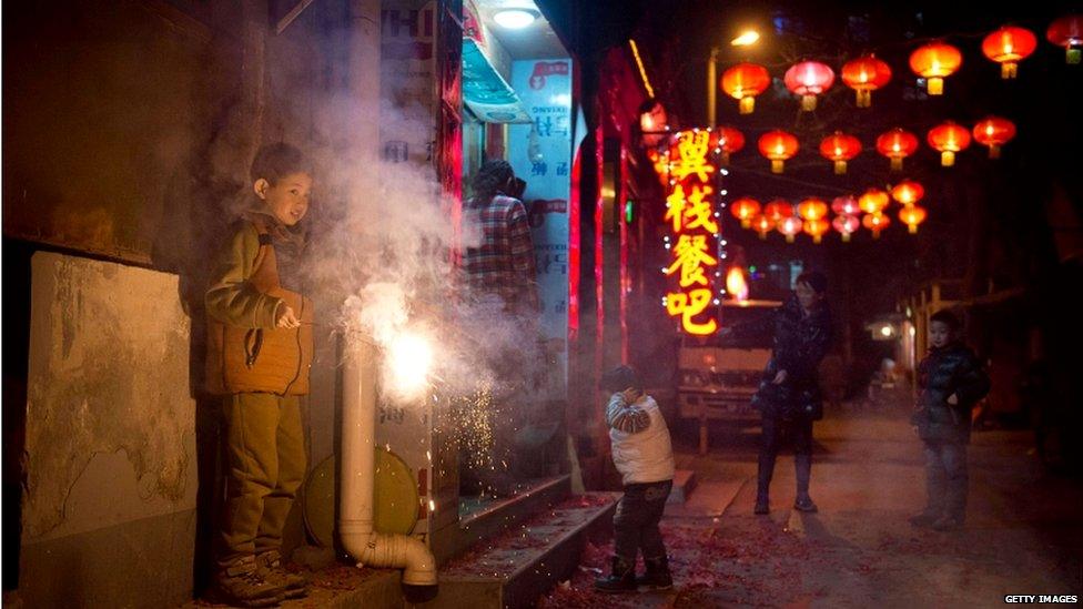 A boy holds a sparkler in an alleyway in Beijing while another covers his ears.