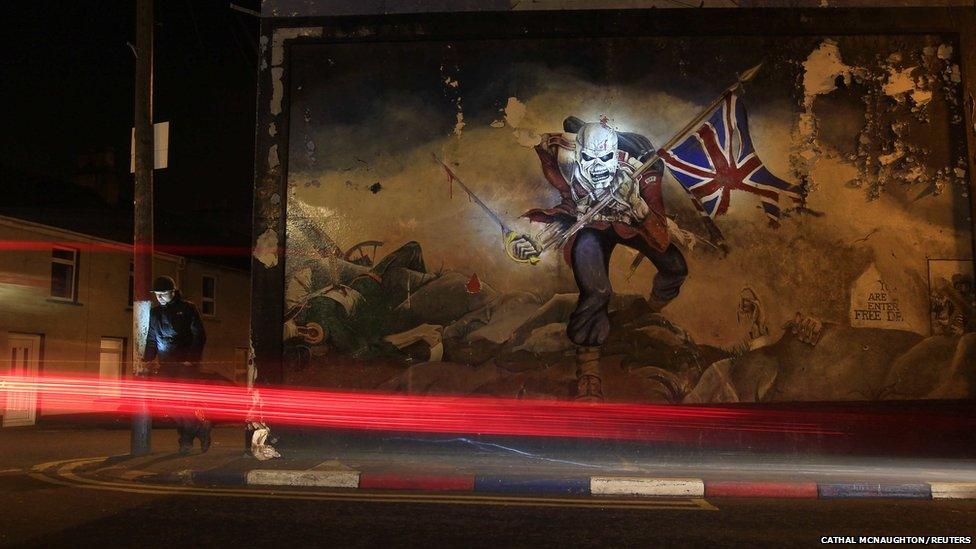 A man checks his mobile phone beside a loyalist paramilitary mural in the Waterside area of Derry