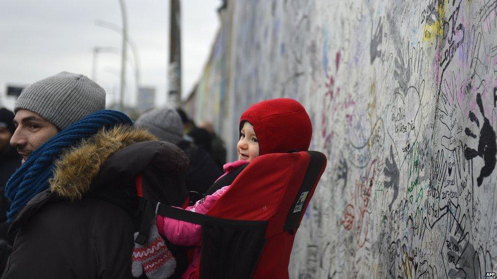 A man and baby stand in front of the Berlin Wall