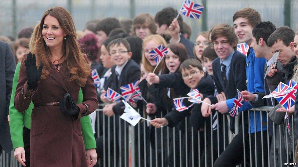 Duchess of Cambridge walking past pupils cheering and waving union jack flags