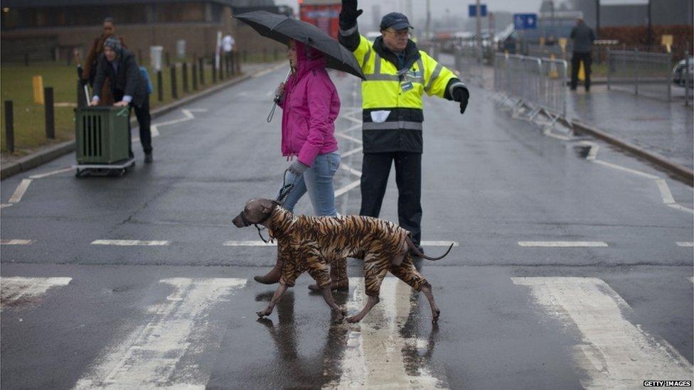 An owner arrives with her dog wearing a waterproof suit on the first day of the Crufts dog show in Birmingham