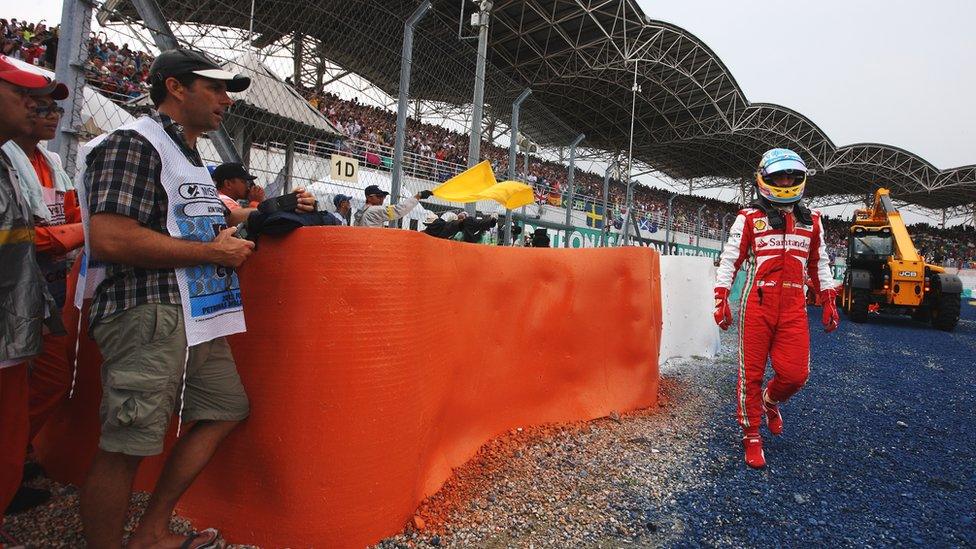 Fernando Alonso walks back while his car is recovered