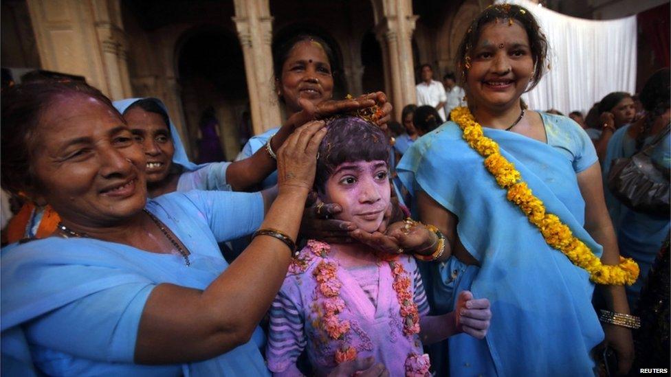 A boy covered in coloured powder poses for pictures with a group of women during a holi celebration at the Meera Sahavagini ashram in Vrindavan, in the northern Indian state of Uttar Pradesh March 24, 201