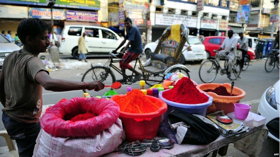 An Indian vendor waits for customers as bowls of coloured powder are displayed at a roadside stall ahead of Holi festival in Allahabad on March 24, 2013.