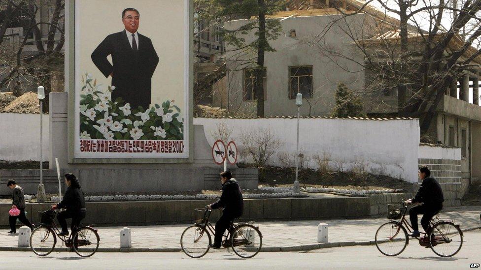 North Koreans ride past a poster of the late leader Kim Il-Sung in the town of Kaesong, 27 March 2005.