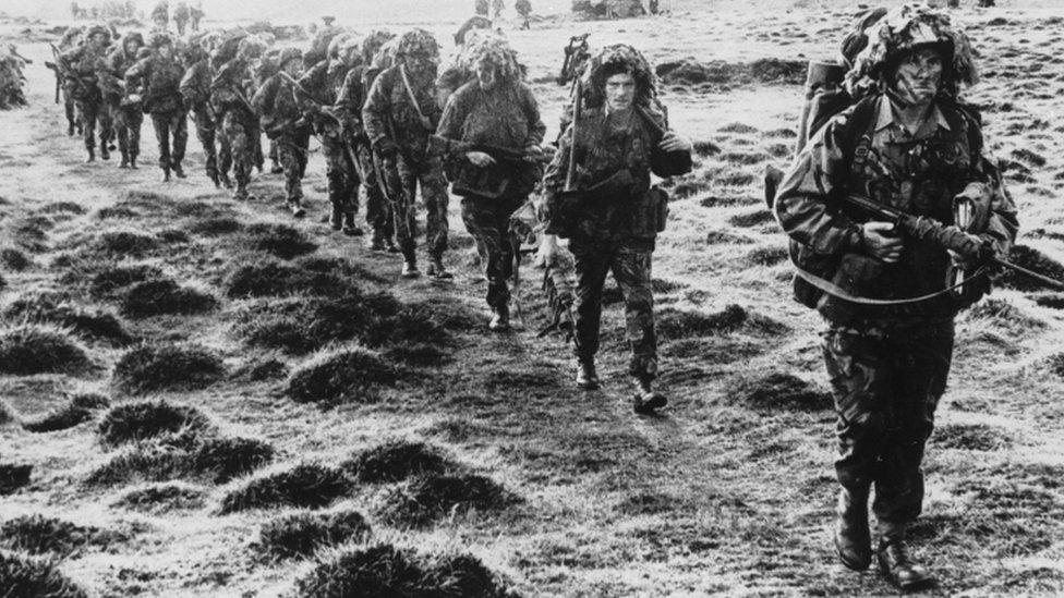 A line of British soldiers in camouflage advancing during the Falklands War