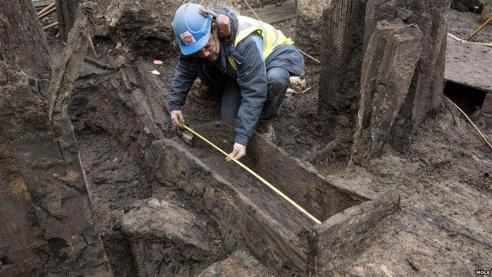 Man measuring a wooden drain buried deep in the mud