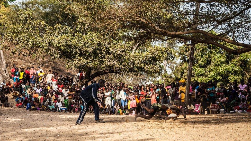 Two people wrestle while referee and crowd watch