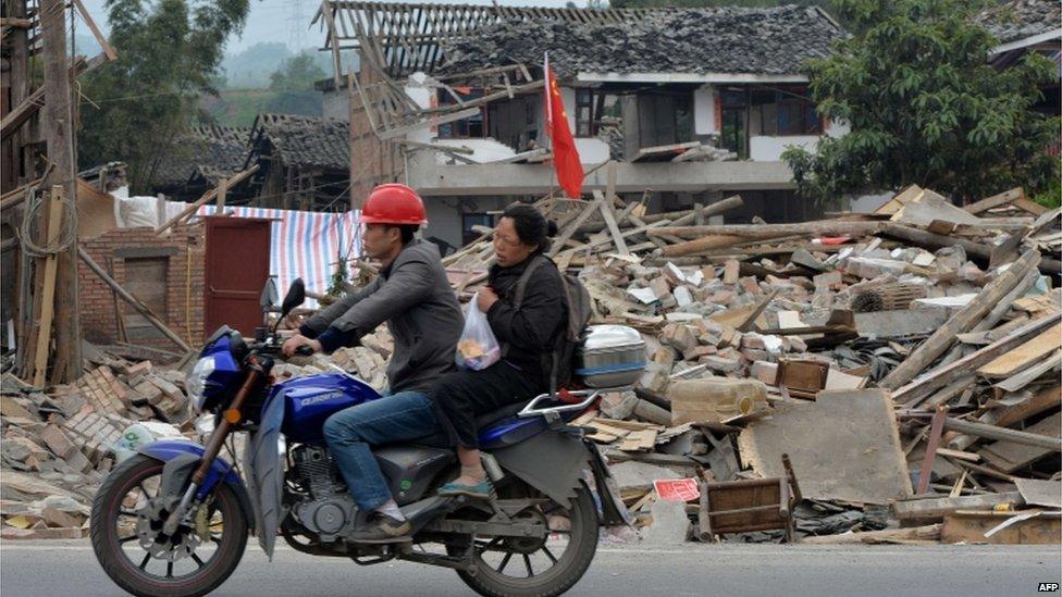 A couple on a motorbike pass flattened houses in Lushan, Sichuan (21 April 2013)