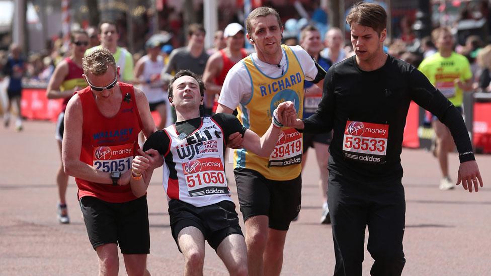 Three runners help another cross the line