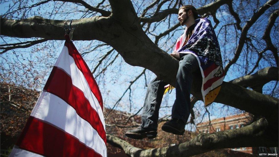 A mourner draped in the US flag watches on from a tree branch before the funeral for Krystle Campbell in Medford, 22 April