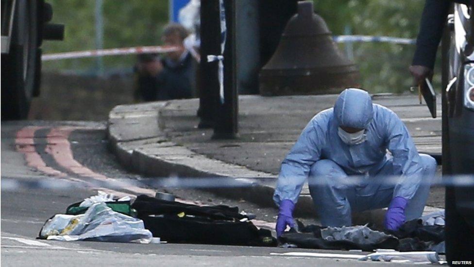 An police forensic investigator in a blue overall and white mask examines the ground