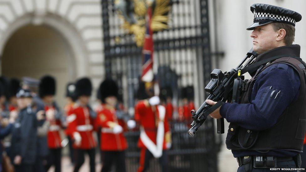 An armed police officer stands guard as British soldiers march through a gate