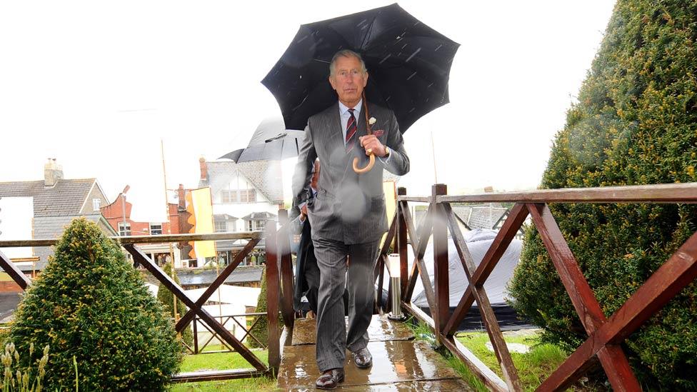 Prince Charles walks holding an umbrella