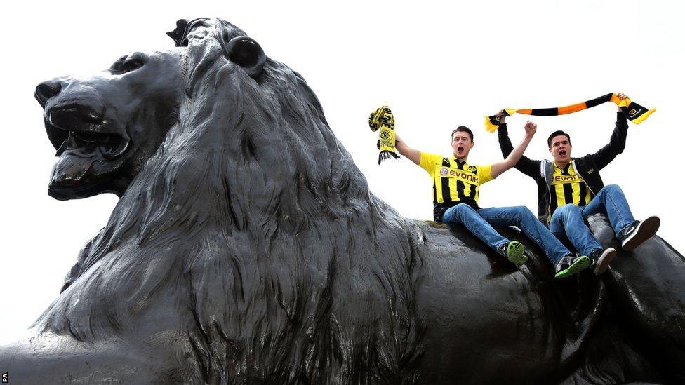 Borussia Dortmund fans on top of one of the lions in Trafalgar Square