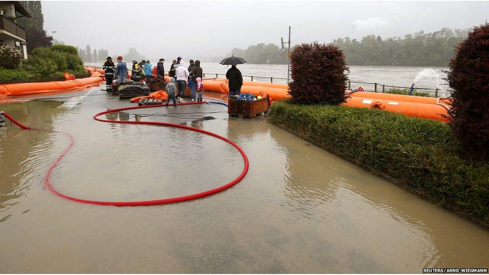 People stand behind a mobile flood protection wall as they look at the floodwater from the Rhine river in the northern Swiss village of Wallbach (June 1, 2013)