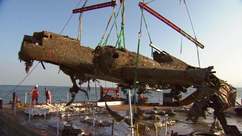 The rusted plane hanging from straps under a crane on a ship