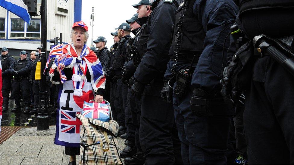 Woman draped in union flag with line of police officers