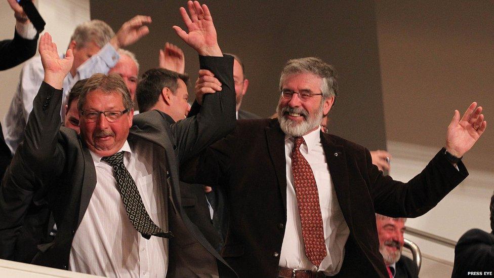 Finance Minister Sammy Wilson and Sinn Fein President Gerry Adams join in a Mexican wave as the gathered crowd await the arrival of President Obama at the Waterfront Hall