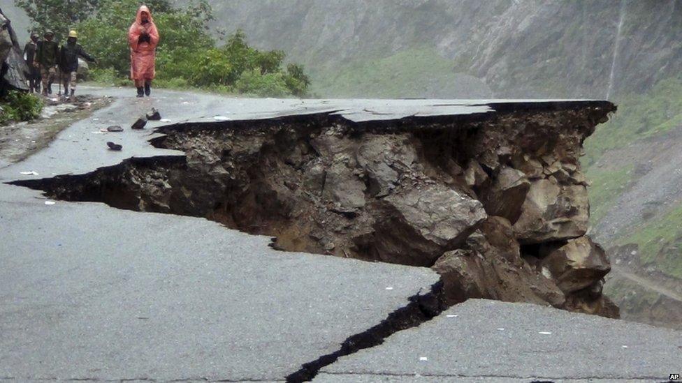 Indian people walk on a road which was caved in after incessant rains on Rishikesh-Mana highway near Joshimath district in northern Indian state of Uttarakhand, India, Monday, June 17, 2013