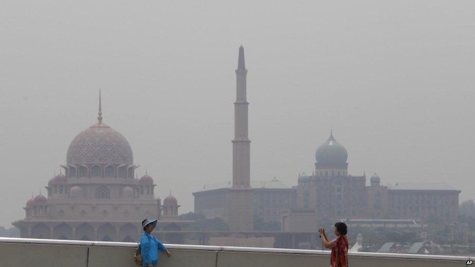 Tourists take a souvenir photo against the background of Putra Mosque, left, and the prime minister's office covered by haze in Putrajaya, Malaysia, 16 June 2013